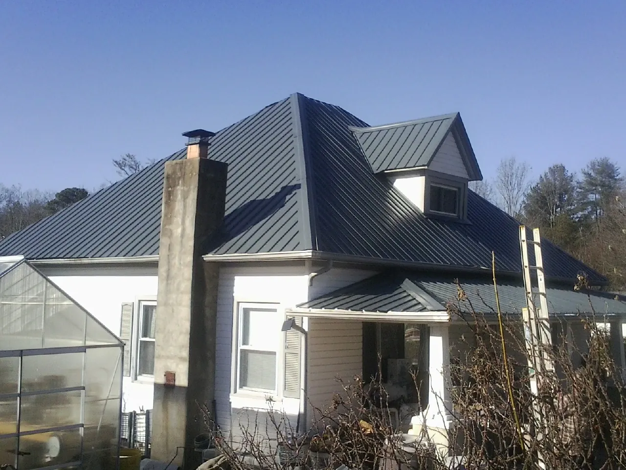 Dark blue standing seam metal roof on a white farmhouse with dormer — Slate & Tile Roof Repair by Roofing Brothers in Belmond