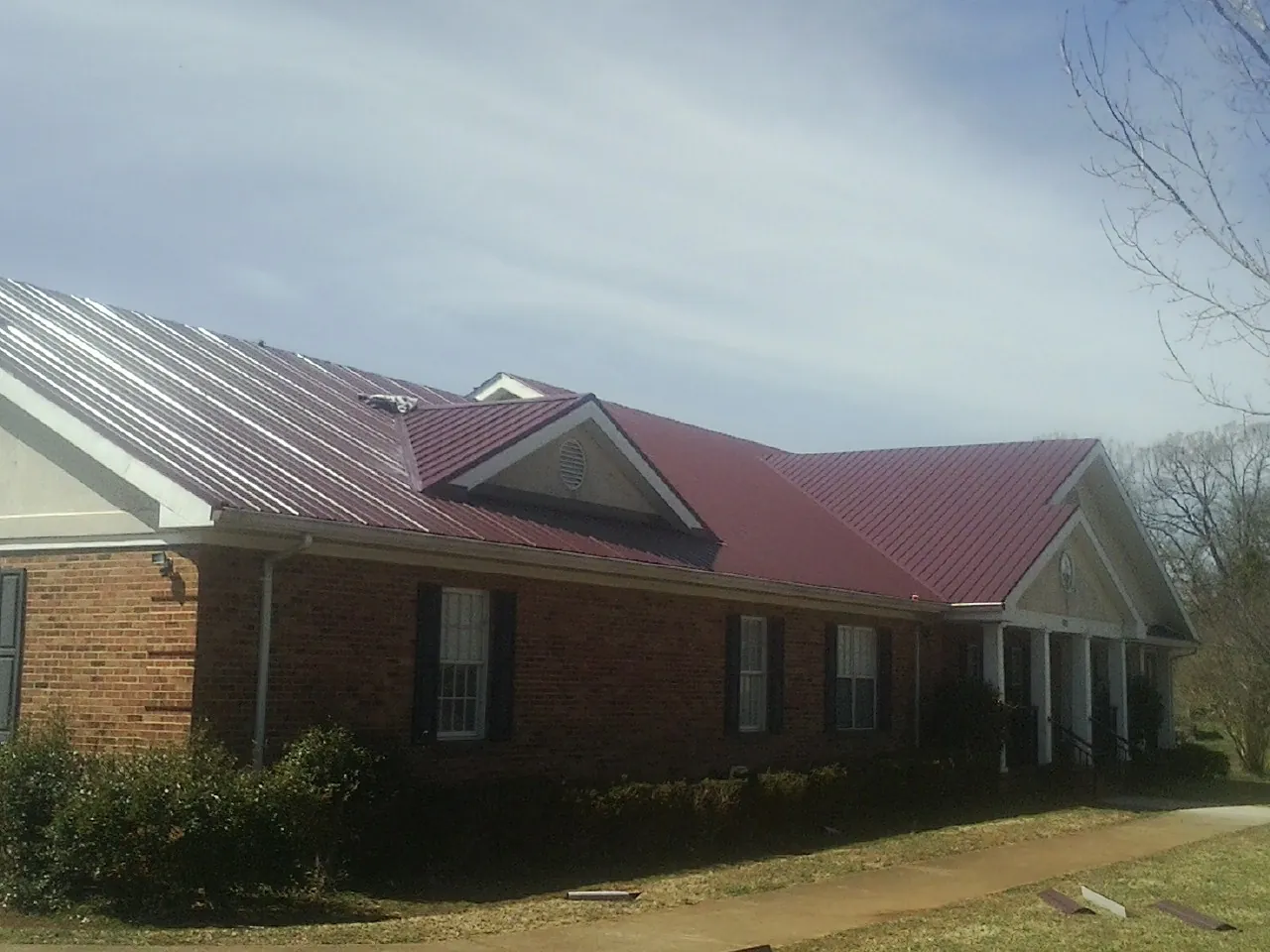 Red metal roof with gabled entries on a long brick building, from a Hail Damage Roof Repair job in Belmond