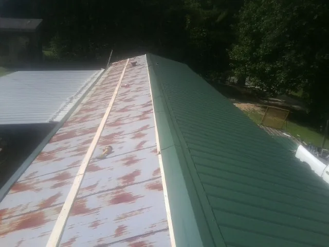 Old rusted panels beside newly installed green metal roofing — Wind Damage Roof Repair by Roofing Brothers in Belmond