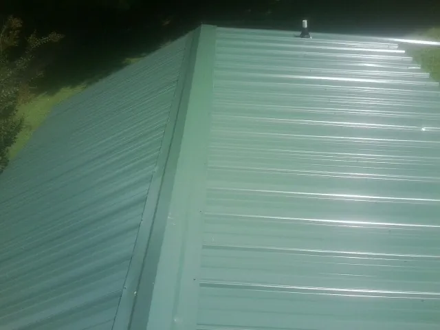 New green metal panels meeting at the ridge of a roof — Flat Roof Repair work by our crew in Belmond