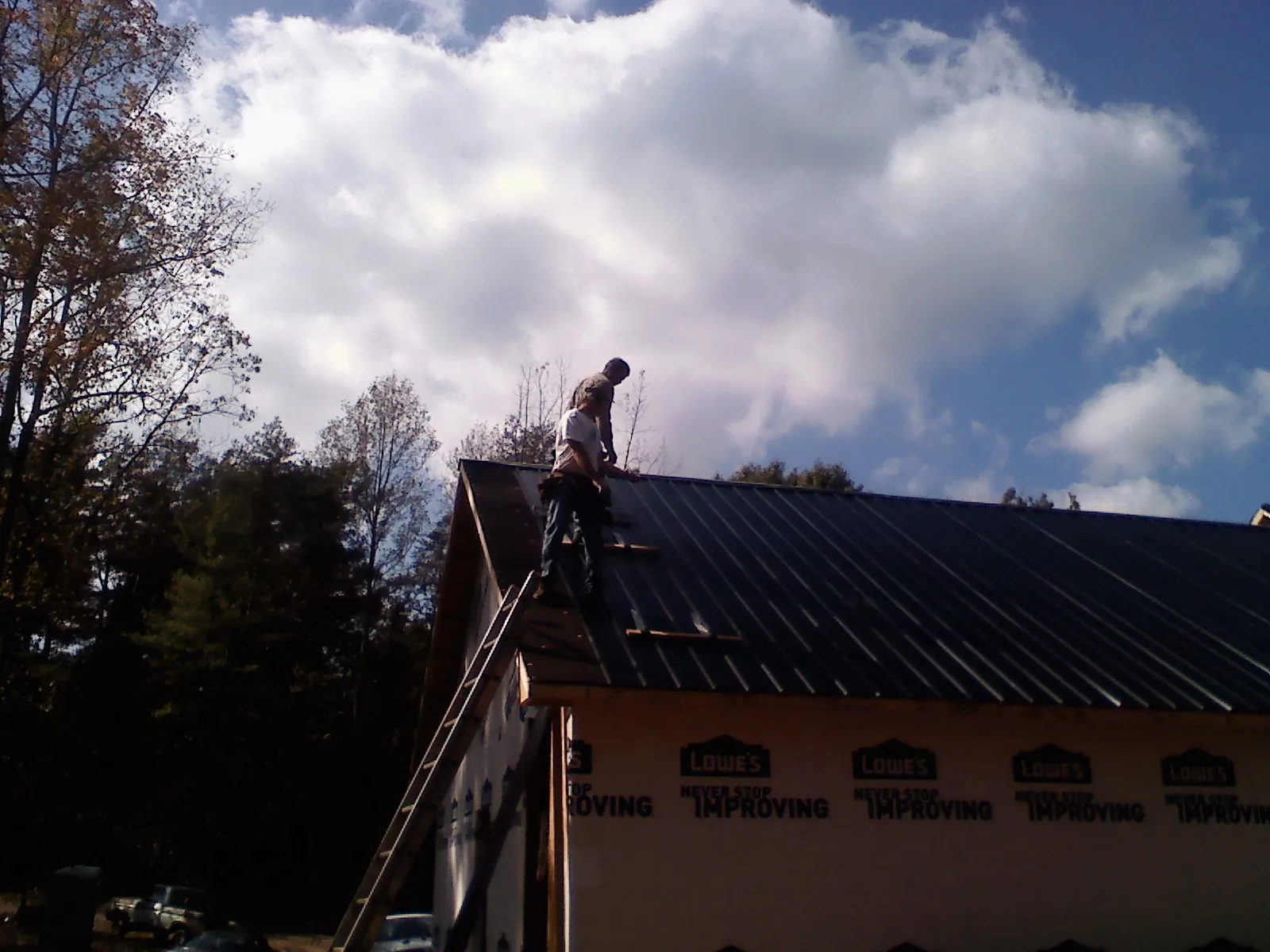 Roofer fastening dark metal panels high against a cloudy sky, from a Roof Inspection job in Belmond