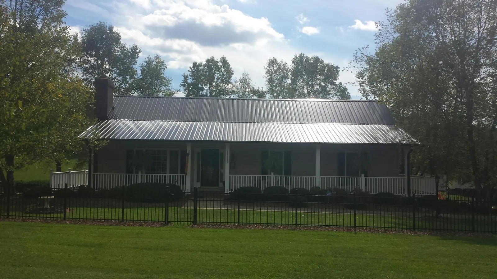 Gray metal roof on a brick ranch with a full width front porch — Gutter Guard Installation work by our crew in Belmond