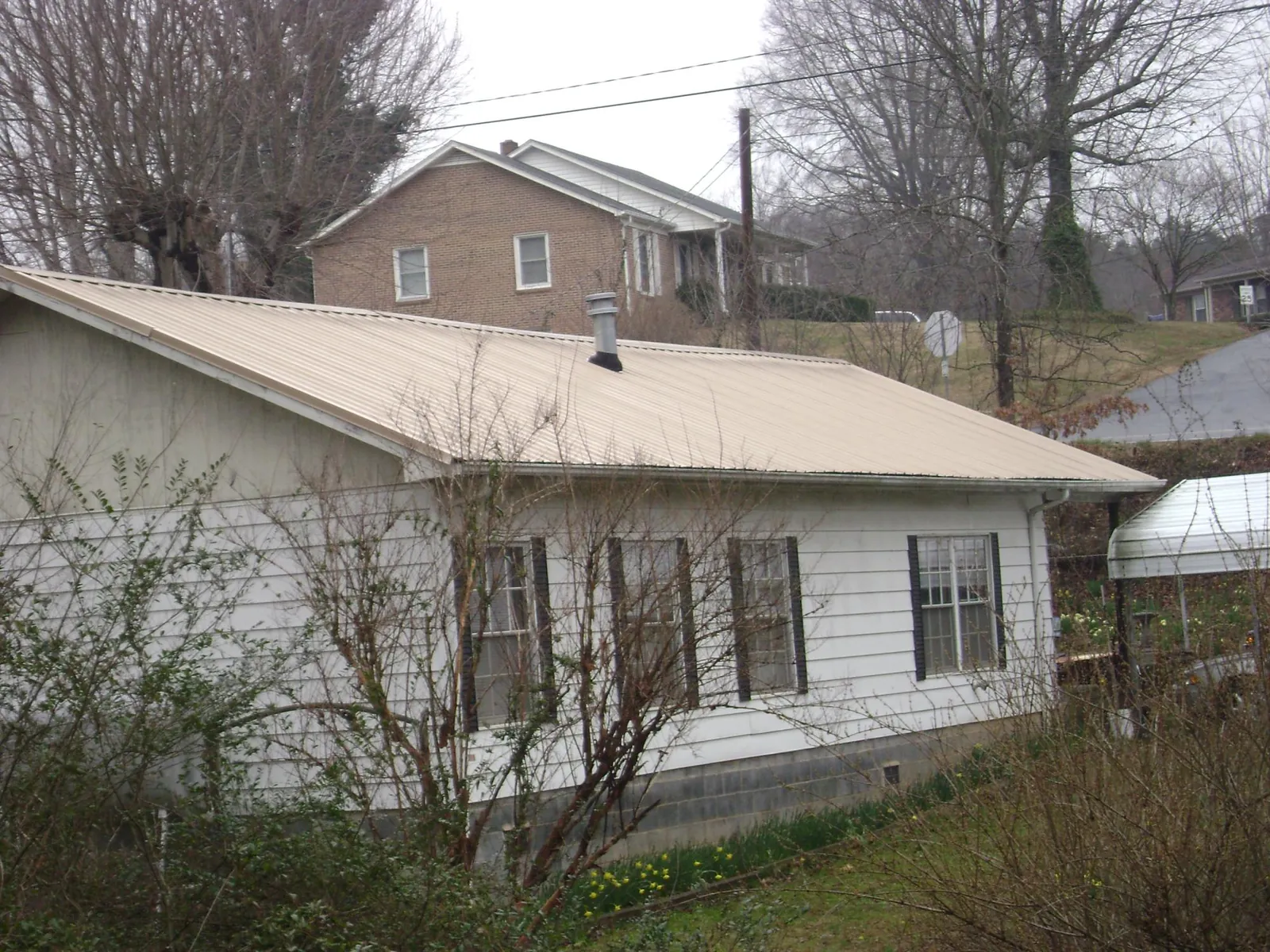 Tan metal roof on a white sided house set into a hillside — Commercial Roofing by Roofing Brothers in Belmond