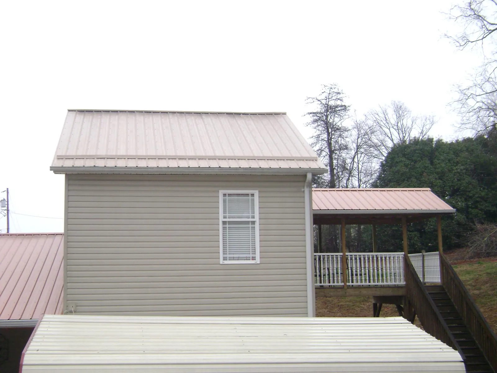 Tan metal roofs on a two story addition and attached porch, from a Roof Replacement job in Belmond