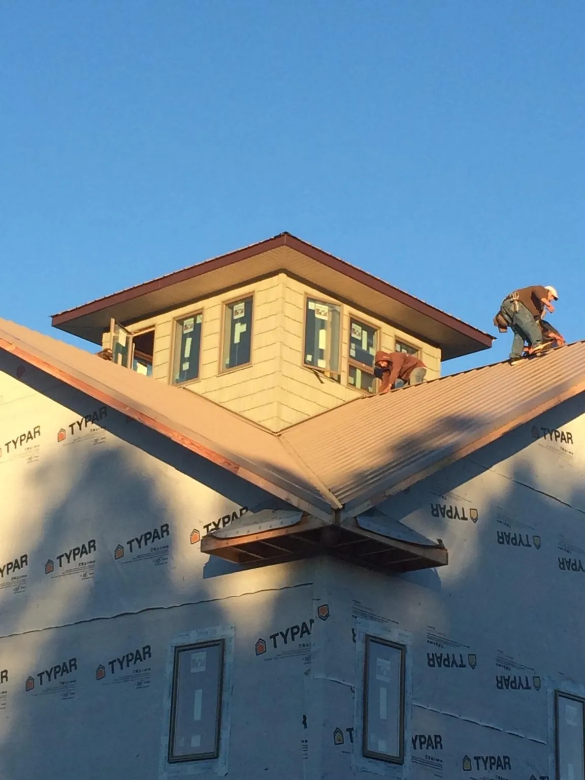 Roofers working around a rooftop cupola on a new metal roof at sunset — Roof Waterproofing in Belmond by Roofing Brothers